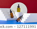 On contrasting color background, red and blue background, white geometries podiums displayed with three amber serum bottles. Container packaging of skin care branding 127111991