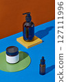 Empty and unlabeled cosmetic bottle decorated with colored platform on contrasting orange and blue background. Scene for product presentation, object placement, cosmetic podium template 127111996