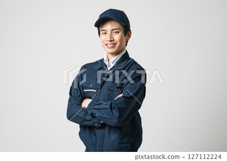 一名 20 多歲的年輕男子身穿工作服,雙臂交叉 一名 20 多歲的年輕男子身穿工作服,雙臂交叉 127112224