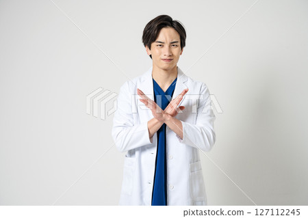 A male doctor in a white coat making a "No" gesture with his hand 127112245