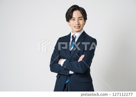 A young man in his 20s wearing a suit with his arms folded 127112277