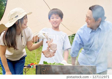 Child lifting grilled meat from a barbecue 127112971