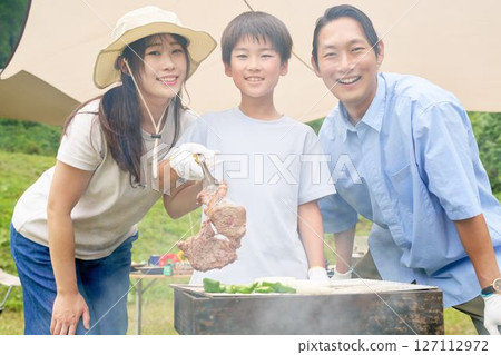 Child lifting grilled meat from a barbecue 127112972