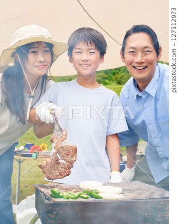 Child lifting grilled meat from a barbecue 127112973