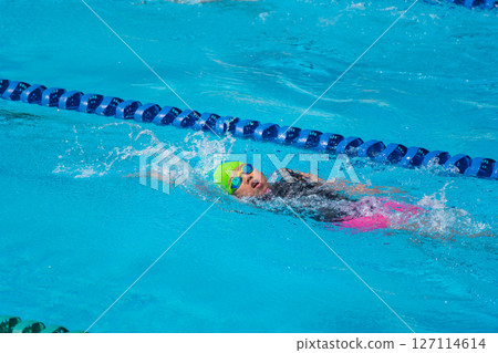 Swimmer child swims backstroke swimming style in a race swimming pool. Water sports and competition, learning to swim classes for children. Swimmer child swims backstroke swimming style in a race swimming pool. Water sports and competition, learning to swim classes for children. 127114614