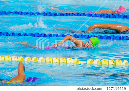 Swimmer child swims freestyle swimming style in a race swimming pool. Water sports and competition, learning to swim classes for children. Swimmer child swims freestyle swimming style in a race swimming pool. Water sports and competition, learning to swim classes for children. 127114619