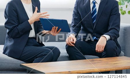 A group of male and female business people discussing business in a lobby while looking at a tablet A group of male and female business people discussing business in a lobby while looking at a tablet 127114845