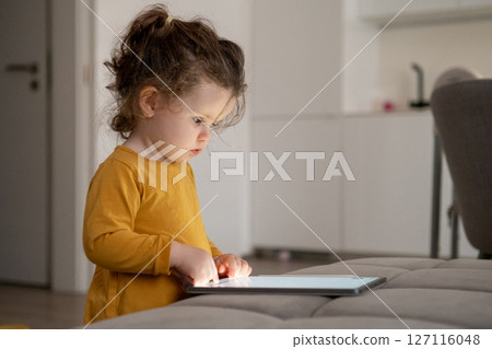 Young girl focused on digital drawing on a tablet. Cozy family space in the background. Young girl focused on digital drawing on a tablet. Cozy family space in the background. 127116048