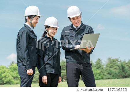 建築工地上，身著工作服的男女工人一邊開會，一邊看著筆記型電腦 127116255