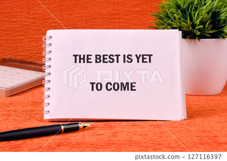 Motivational quotes THE BEST IS YET TO COME on a spiral notebook on an orange background Motivational quotes THE BEST IS YET TO COME on a spiral notebook on an orange background 127116397