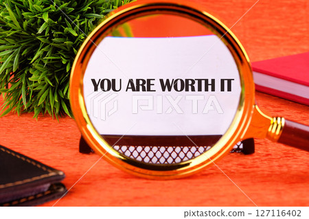 YOU ARE WORTH IT words focuses through a magnifying glass on a business card on an orange background 127116402
