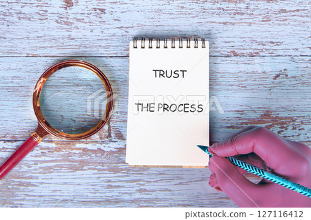TRUST process, business concept. TRUST THE PROCESS words on a handwritten note placed next to a magnifying glass on old boards 127116412