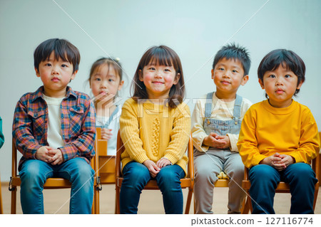 A group of children sitting on wooden chairs in a row 127116774