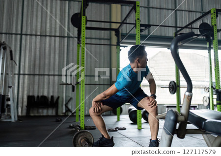 Fitness Workout. Young man performing squats in gym environment. Fitness Workout. Young man performing squats in gym environment. 127117579