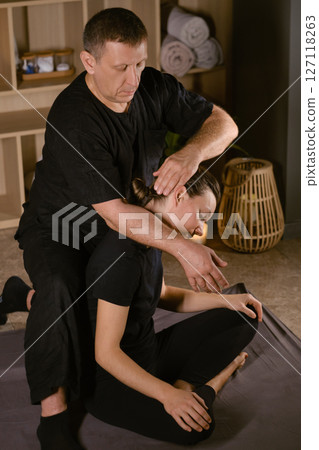 A man gives a Thai neck massage to a girl at a spa. A professional therapist performs a therapeutic neck massage on a girl 127118263