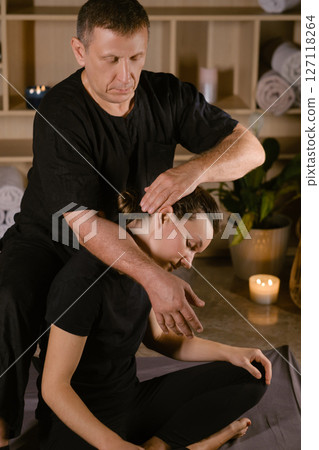 A man gives a Thai neck massage to a girl at a spa. A professional therapist performs a therapeutic neck massage on a girl 127118264