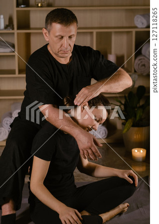 Client in Thai massage session with therapist. A man giving a Thai neck massage to a girl in a spa salon 127118265