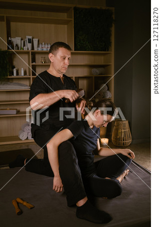 Male master giving Thai Toksen massage to girl in massage room. A girl gets a relaxing Thai back massage with a Toxen massage kit 127118270