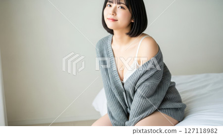 A Japanese female model sitting on a bed in white underwear and a cardigan 127118982