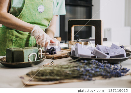 Person stamps lavender soap near dried flowers and green bars in a small workshop. Aromatherapeutic soap, functional wellness, lavender benefits, plant-based fragrance Person stamps lavender soap near dried flowers and green bars in a small workshop. Aromatherapeutic soap, functional wellness, lavender benefits, plant-based fragrance 127119015