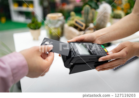 A person pays for purchases at a florist shop by using a credit card with a contactless payment terminal. A person pays for purchases at a florist shop by using a credit card with a contactless payment terminal. 127119203