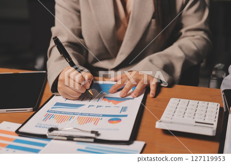 Group of confident business people point to graphs and charts to analyze market data, balance sheet, account, net profit to plan new sales strategies to increase production capacity. 127119953