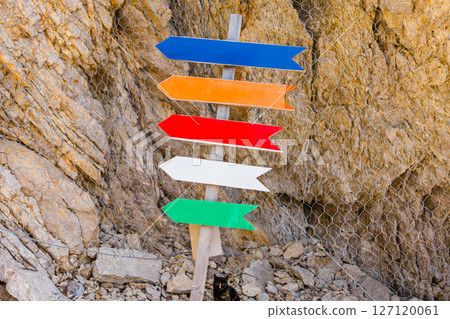 Colorful wooden arrows pointing in different directions on rocky background, copy space. Navigation, outdoor signage, and playful wayfinding in natural setting. 127120061