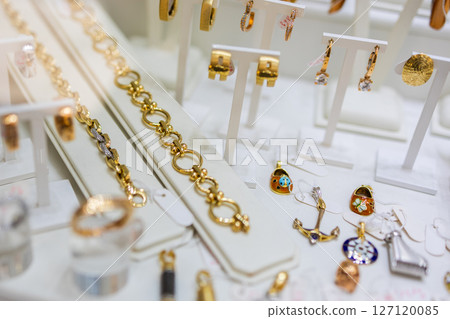 Gold bracelets, earrings, and charms arranged in jewelry store display. Luxury fashion, accessory detail, and elegant retail collection. 127120085