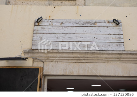 Blank weathered wooden signboard mounted above shop entrance. Vintage texture, urban signage, and rustic commercial exterior. 127120086