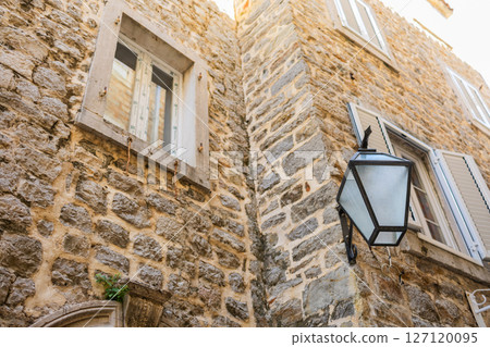 Stone facade of old European building with vintage street lamp. Urban architecture, historical texture, and traditional window design. Stone facade of old European building with vintage street lamp. Urban architecture, historical texture, and traditional window design. 127120095