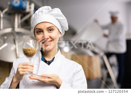 Female brewmaster holding glass of malt seeds Female brewmaster holding glass of malt seeds 127120354