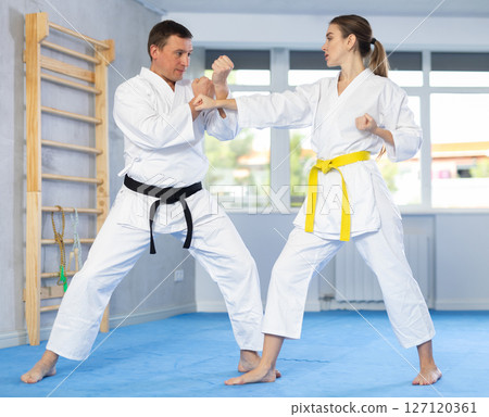 Sparring woman and man in white kimono during karate training in gym Sparring woman and man in white kimono during karate training in gym 127120361