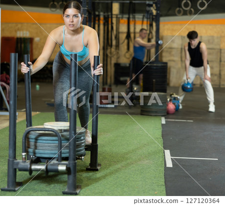 Motivated strong young woman in activewear cross fit equipment on artificial grass turf in gym. CrossFit healthy concept 127120364