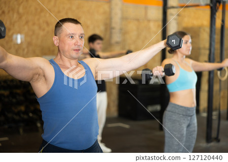 Focused man pumping up deltoid muscles with dumbbells in gym Focused man pumping up deltoid muscles with dumbbells in gym 127120440