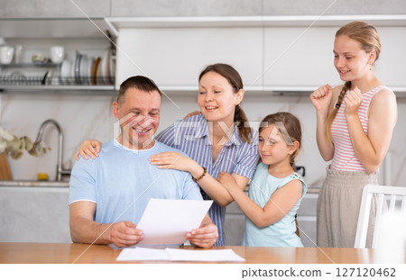 Happy man with wife and teenage daughters reading notification at home 127120462