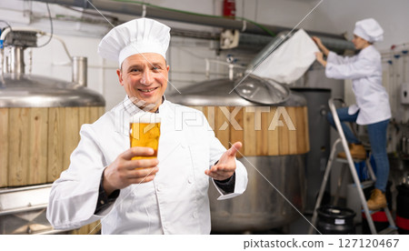 Satisfied professional brewer holding out glass with craft beer 127120467