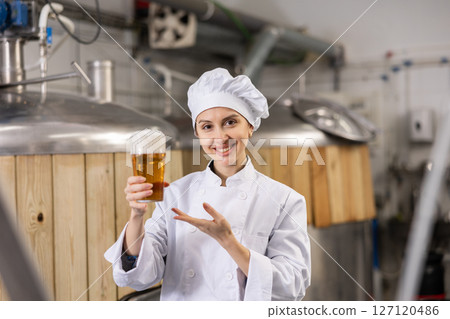 Portrait of female brewer who is standing with glass of beer on his workplace in brew-house 127120486