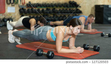 Young girl holding plank pose during bodyweight workout in gym 127120503