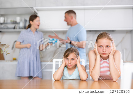 Distraught teenage girls suffering from parents conflict sitting in kitchen Distraught teenage girls suffering from parents conflict sitting in kitchen 127120505