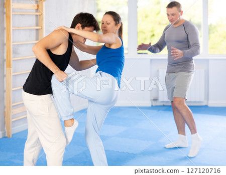 Self-defense class - a woman practices blows to the head of an attacking man under the guidance of trainer Self-defense class - a woman practices blows to the head of an attacking man under the guidance of trainer 127120716
