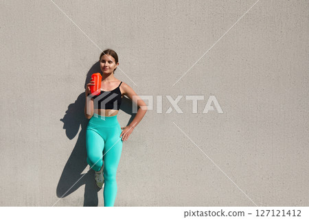 Fitness enthusiast holding a protein shake while leaning against a wall in stylish activewear promoting a healthy lifestyle and fitness motivation concept Fitness enthusiast holding a protein shake while leaning against a wall in stylish activewear promoting a healthy lifestyle and fitness motivation concept 127121412