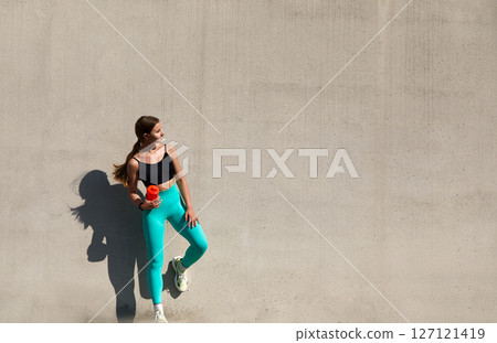 Beautiful fitness athlete woman drinking water after work out exercising. Woman drinking water from bottle.  Female drinking water after exercises or sport. Sports woman in active wear standing 127121419