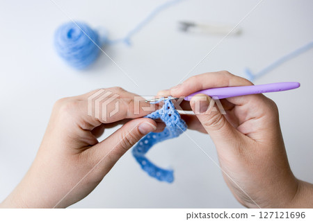 Close up of crocheting hands with purple hook and blue yarn 127121696