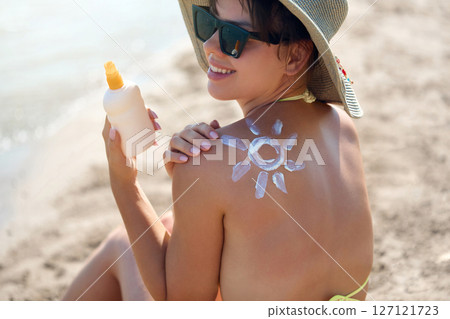Sun cream on tanned shoulder with sun shape . Sun protection. Beautiful woman in bikini applying  Solar Cream. Skin and body care.Portrait of female holding suntan lotion 127121723