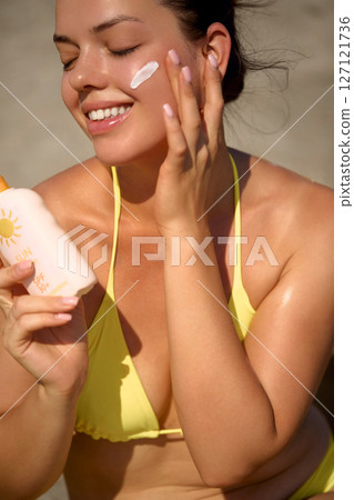 Sun cream on tanned shoulder with sun shape . Sun protection. Beautiful woman in bikini applying  Solar Cream. Skin and body care.Portrait of female holding suntan lotion 127121736
