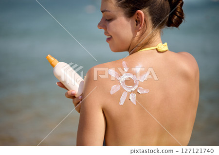 Sun cream on tanned shoulder with sun shape . Sun protection. Beautiful woman in bikini applying  Solar Cream. Skin and body care.Portrait of female holding suntan lotion 127121740