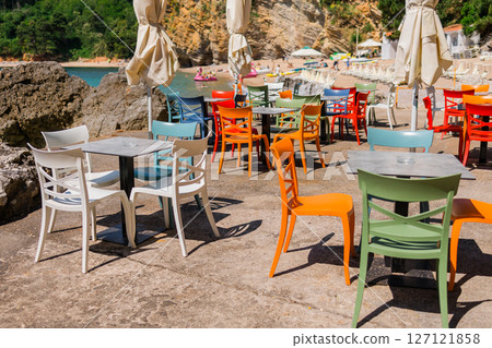 Colorful plastic chairs arranged in a seaside cafe setting. Outdoor dining, summer leisure, and vacation relaxation near the beach. 127121858