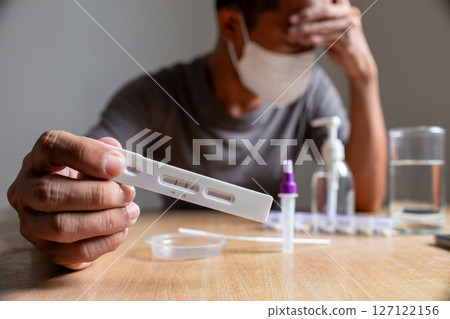 Distressed man holds a positive COVID-19 rapid antigen test result, showing emotional impact 127122156