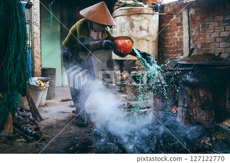 Vietnamese female worker puts out a fire in furnace in a reed dyeing workshop at factory in a village. Asian woman does dirty hard men's work in a factory in Asia 127122770