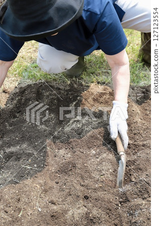 一位老年婦女在施肥後用鏟子平整菜園裡的土壤 127123554